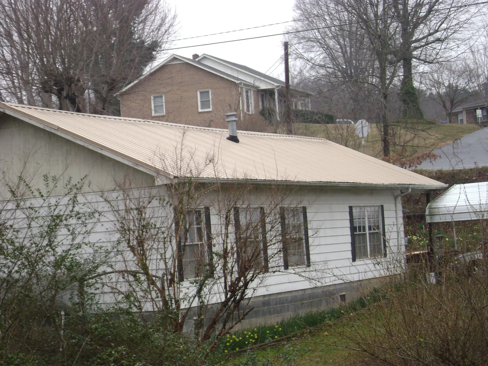 Tan metal roof on a white sided house set into a hillside — Commercial Roofing by Roofing Brothers in Stockbridge