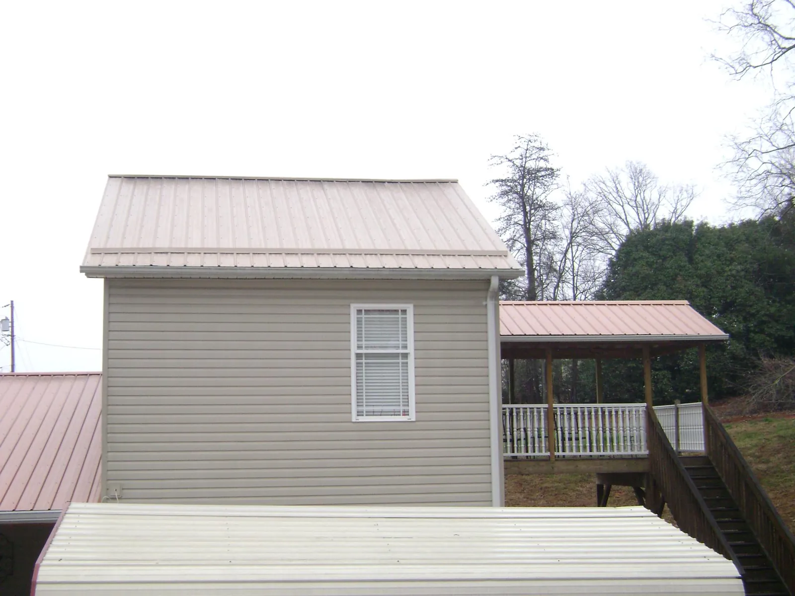 Tan metal roofs on a two story addition and attached porch, from a Roof Replacement job in Stockbridge